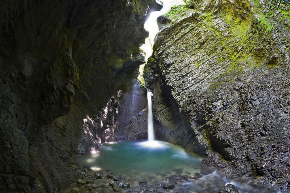 Waterfall Kozjak gushes over a rocky ledge into an emerald green pool below