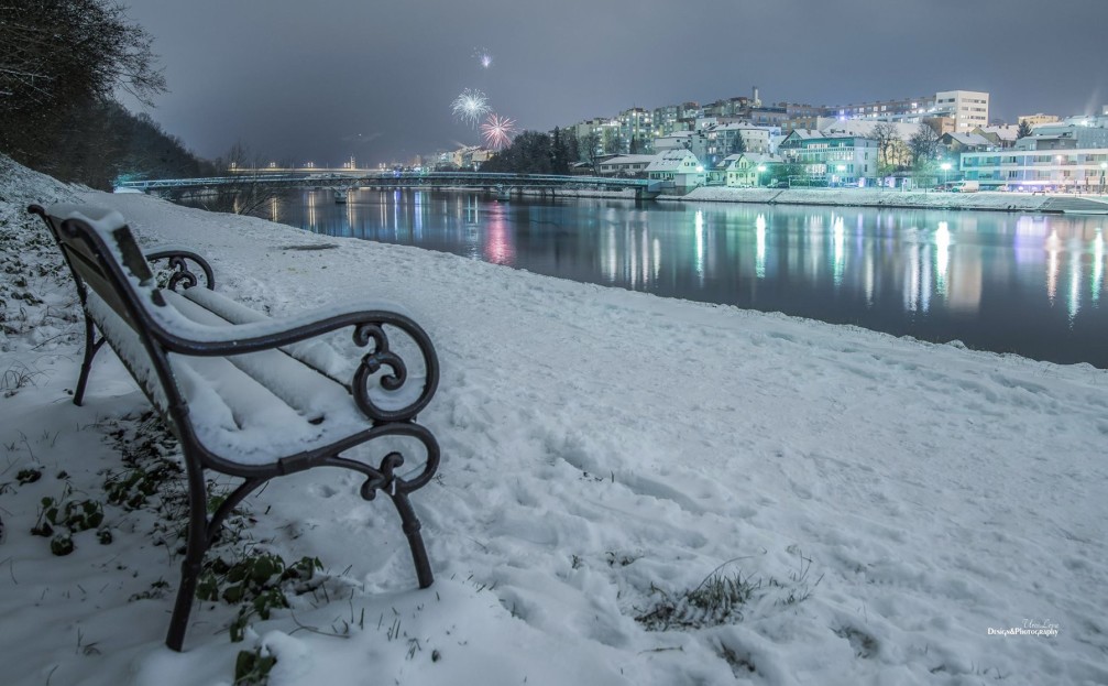 Path and one of many benches along the Drava river in winter in Maribor, Slovenia