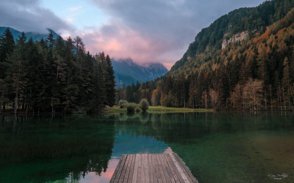 Lake Plansarsko Jezero, emerald green and surrounded by meadows and majestic mountains in Jezersko, Slovenia