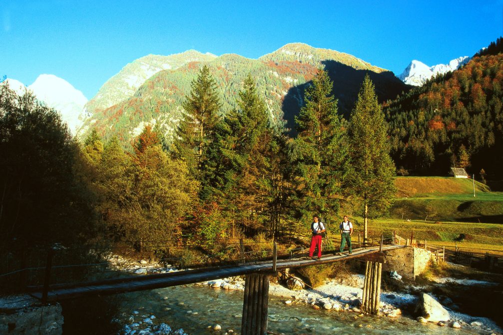 Two hikers crossing the wooden footbridge over the Soca river in the Trenta Valley in Slovenia