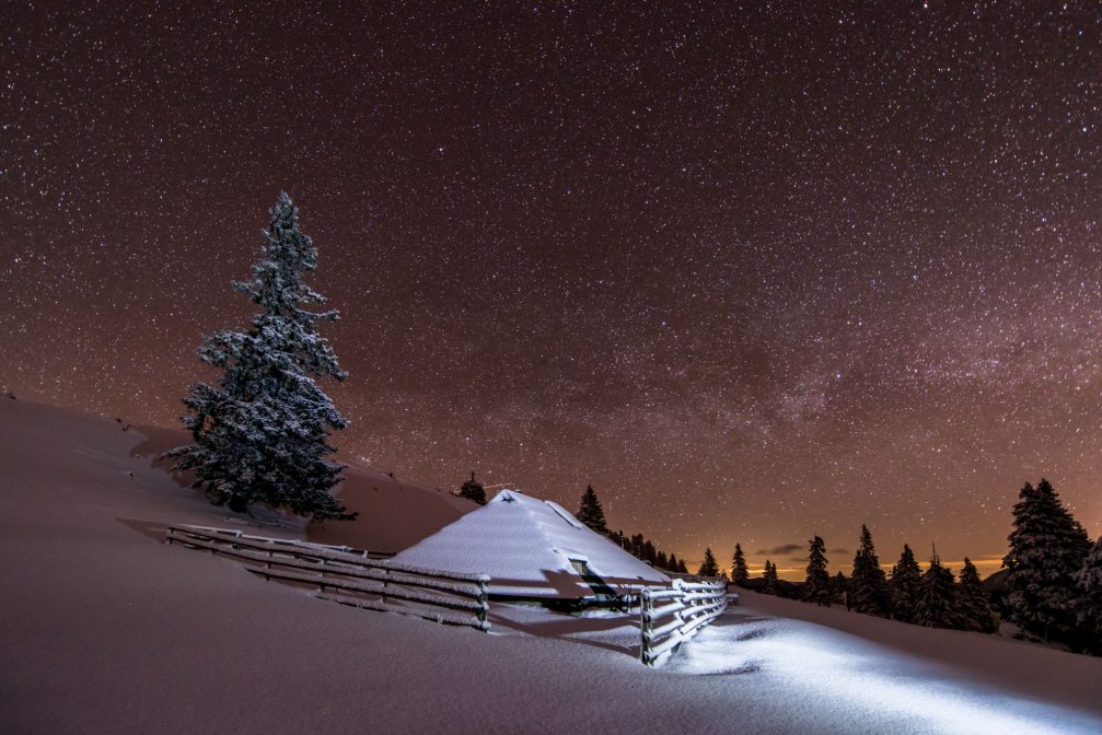 A unique, shingle-roofed wooden hut at Velika Planina at night covered with snow in the winter