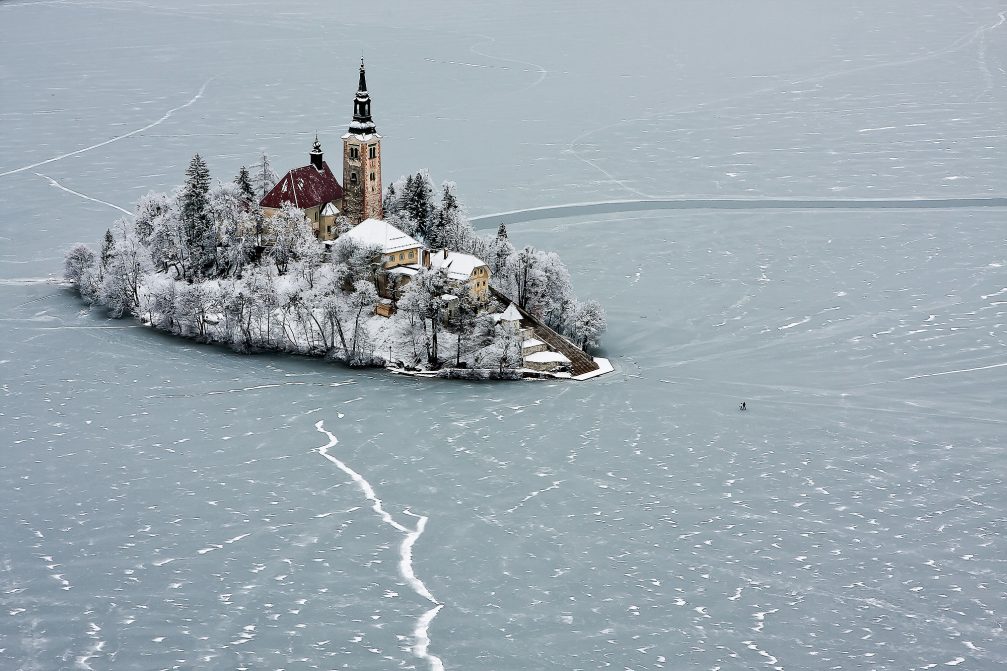 Frozen Lake Bled in the winter time with people walking on the ice to the island with a church