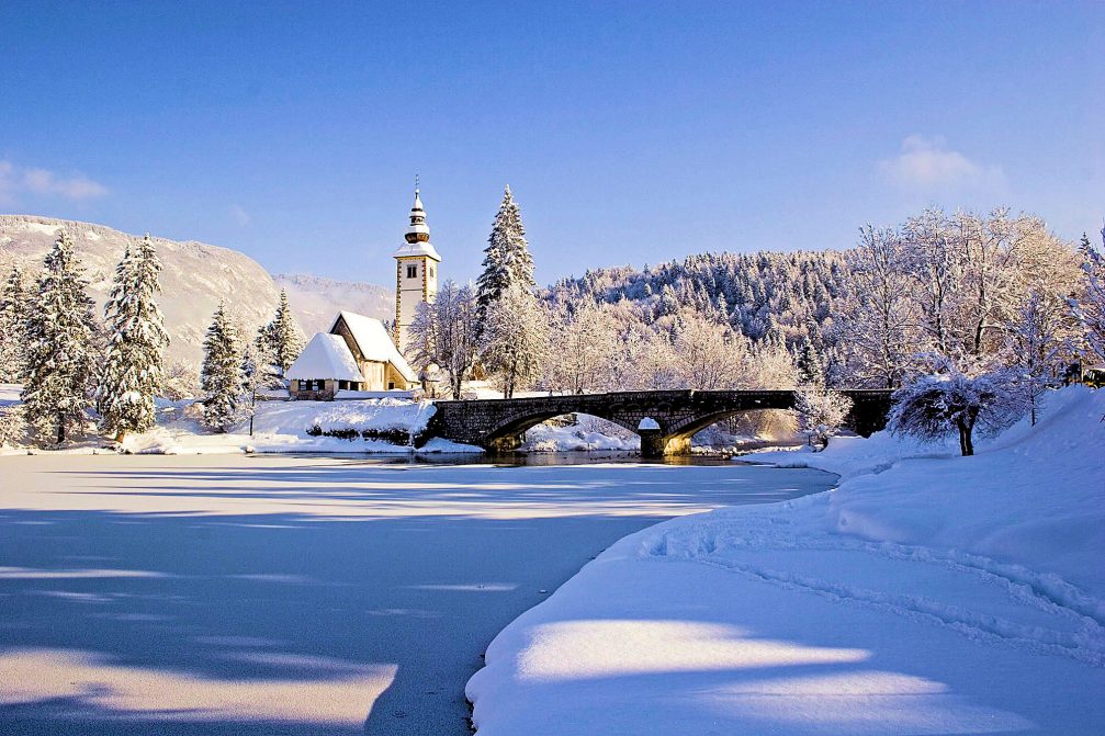 Frozen Lake Bohinj in the winter time with a church and stone bridge in the background