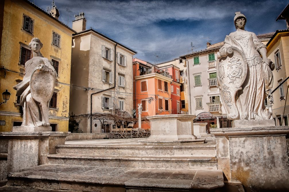 Figures of law and justice on either side of the stairs in the First Of May Square in Piran