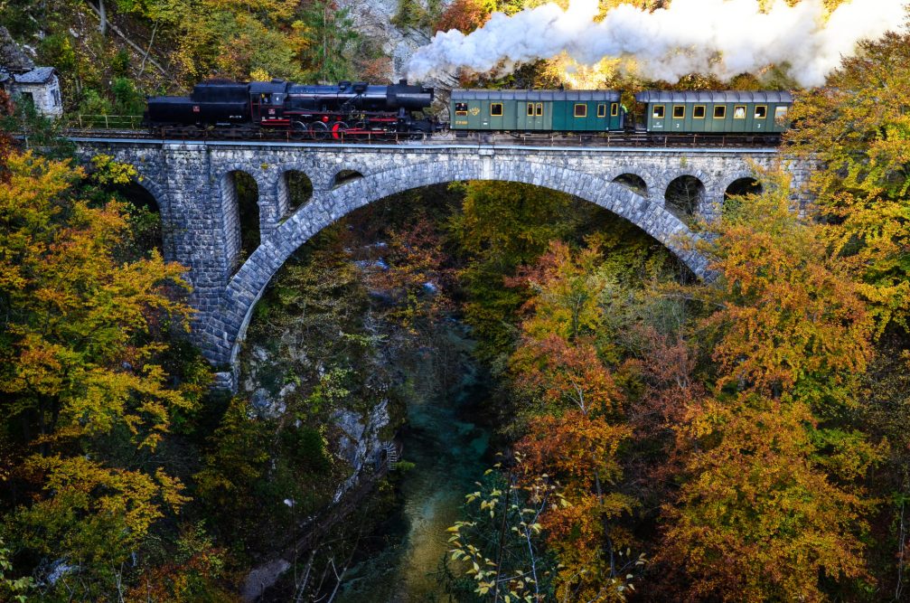 A steam-powered museum train crossing an old bridge above the Vintgar Gorge near Bled in autumn