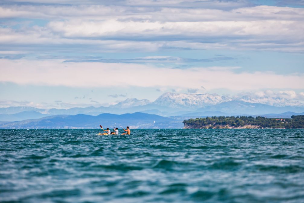 Rowers in the Koper bay with Debeli Rtic and the Julian Alps in the background