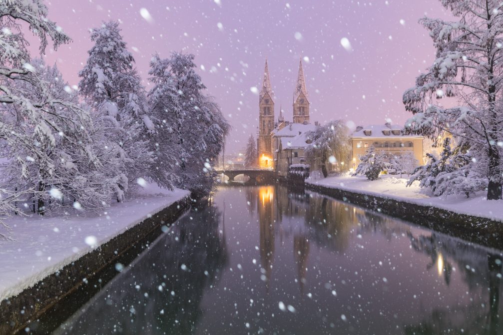 River Rinza flowing next to the parish church of St Bartholomew in Kocevje in southeastern Slovenia in the winter while snowing