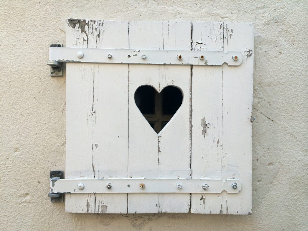 A detail of white wooden window shutter with carved out heart in Slovenia