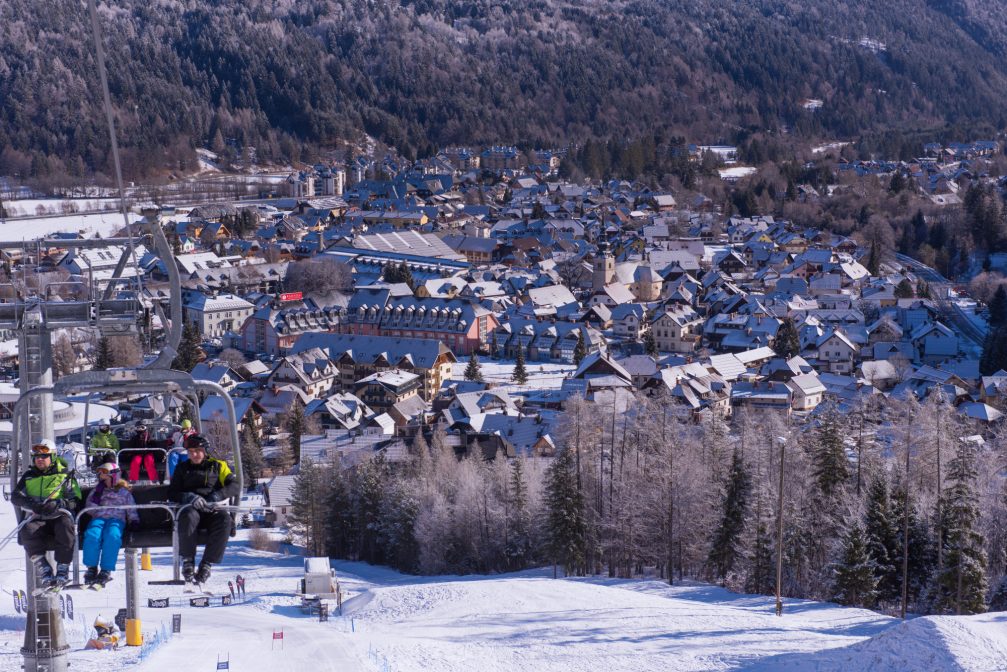 Skiers going up the slopes on a chair lift at Kranjska Gora Ski Resort with the village of Kranjska Gora