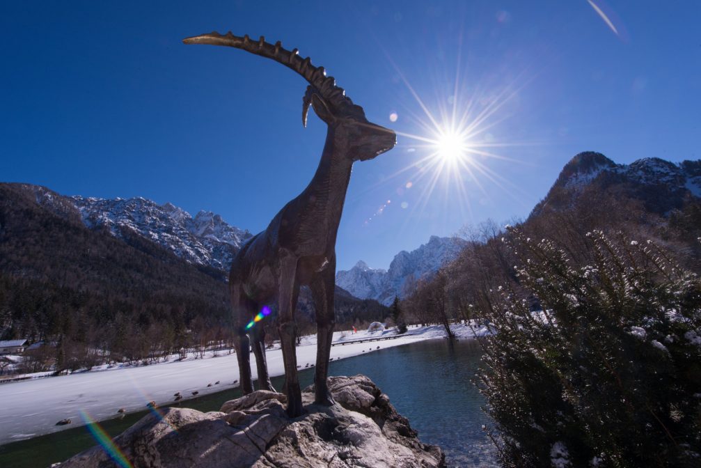 A statue of Zlatorog goldhorn on a boulder in front of Lake Jasna in the winter