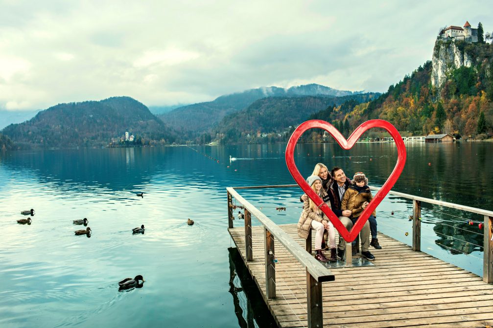 A family on a wooden pier with a big red heart at Lake Bled in the autumn