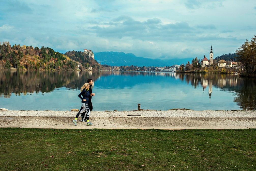 A couple jogging around Lake Bled in the autumn with Bled Castle in the background
