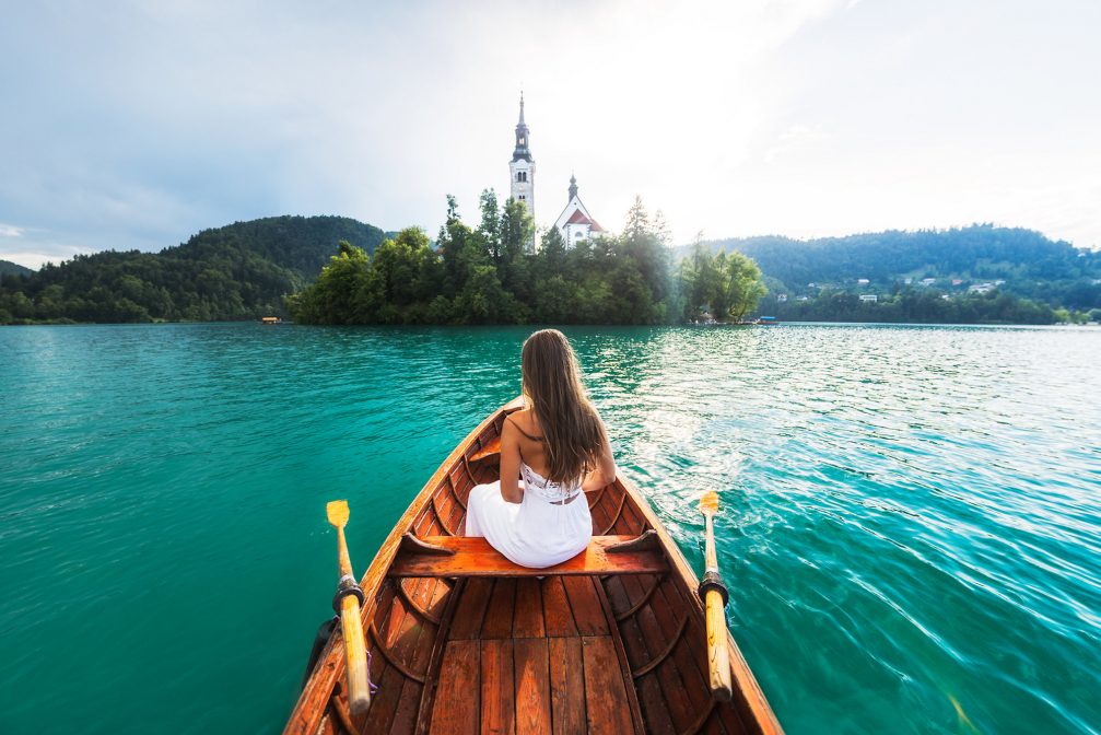 A bride in a wooden row boat with Bled Island in the background
