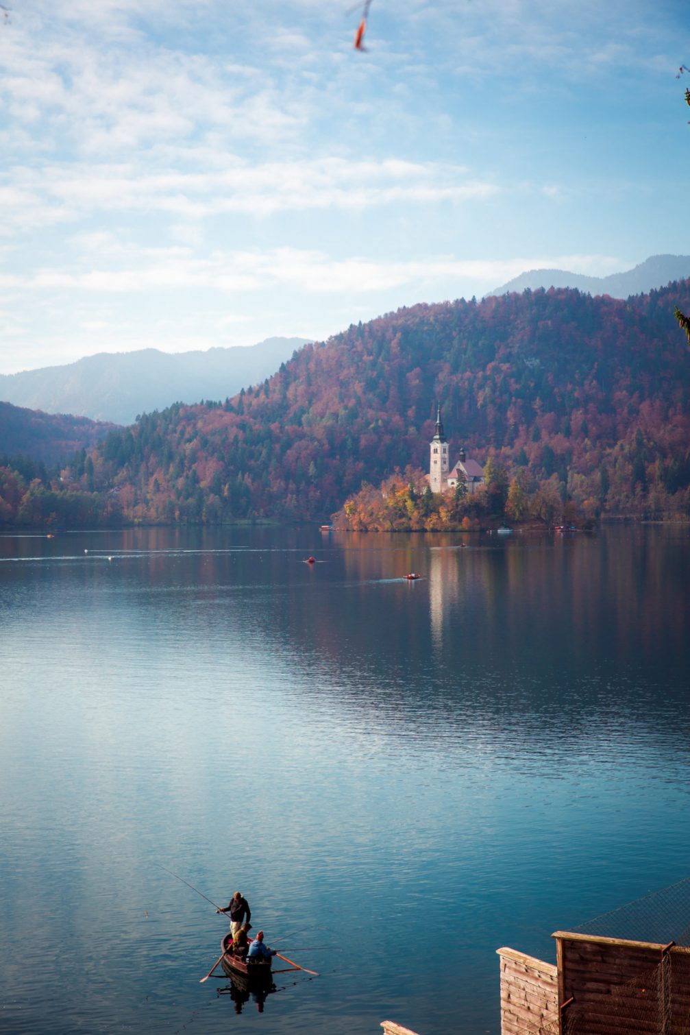 A man in a boat fishing in Lake Bled with Bled Island in the background