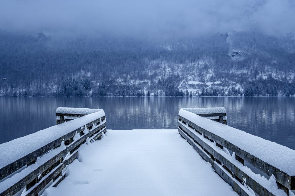 Wooden pier covered in snow leading into Lake Bohinj on a dull day in winter