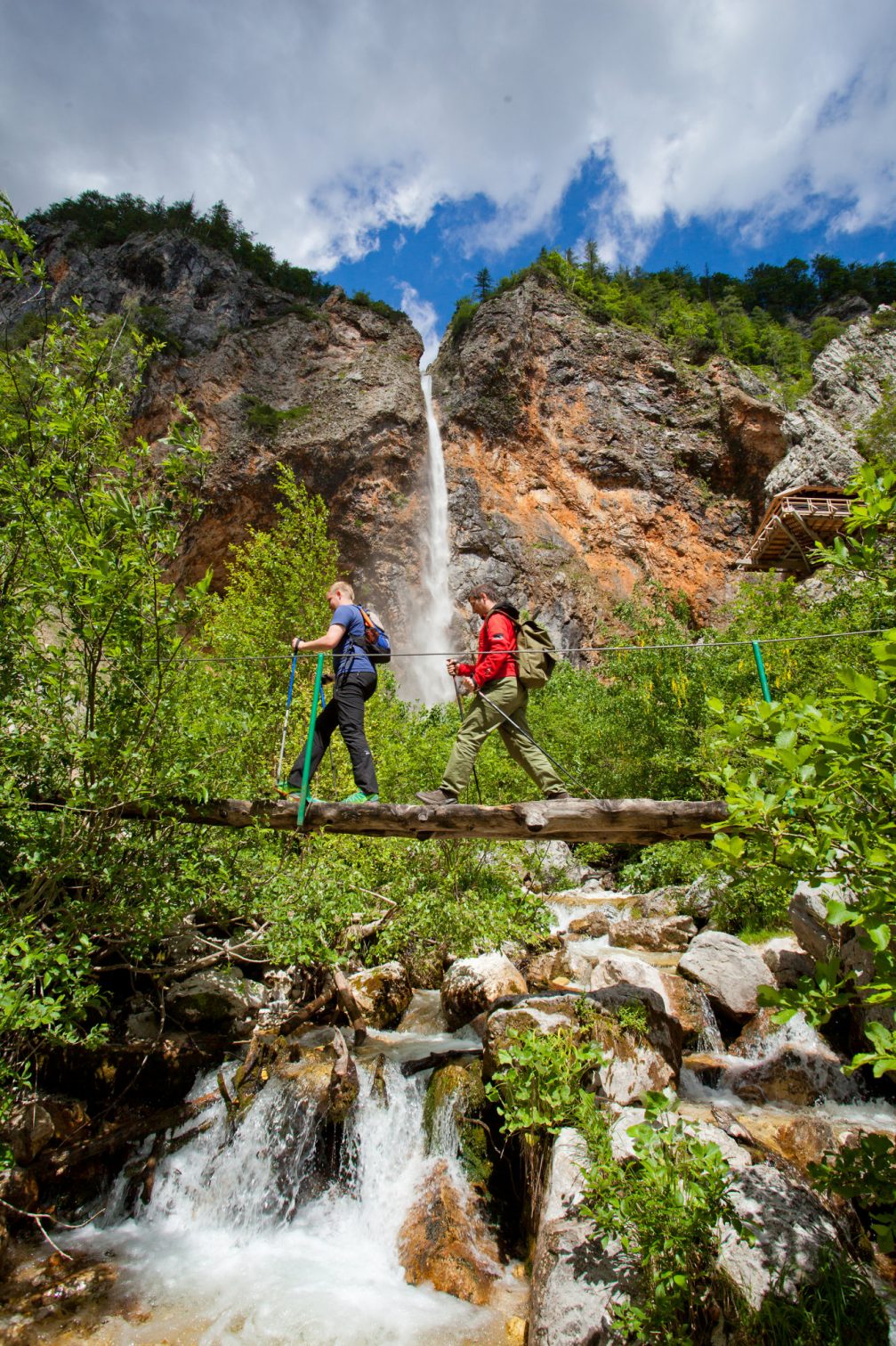 A couple of hikers crosing the bridge with Rinka Waterfall in the background