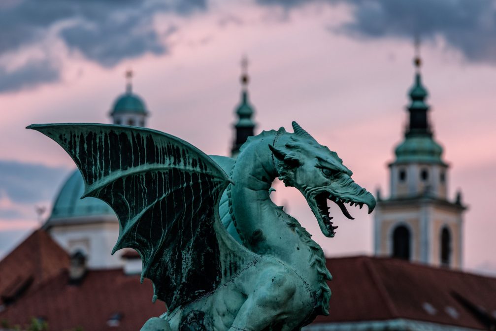 Statue of a dragon at Dragon Bridge with Ljubljana Cathedral in the background