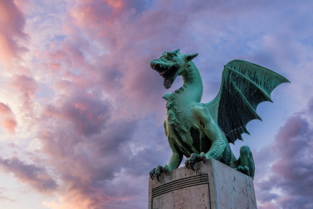 A statue of dragon on the Dragon Bridge in Ljubljana at sunset