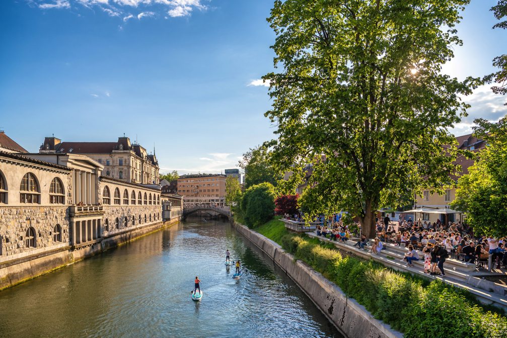 Stand up paddle boarders on Ljubljanica River at Petkovskovo Embankment in Ljubljana