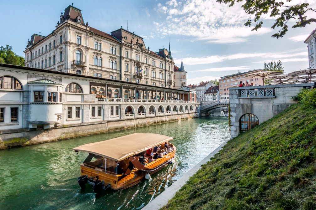 A tourist boat on River Ljubljanica with Plecnik Covered Market in Ljubljana in the background