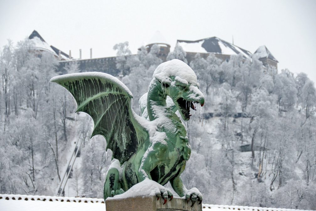 A statue of dragon covered in snow on Dragon Bridge in Ljubljana in winter