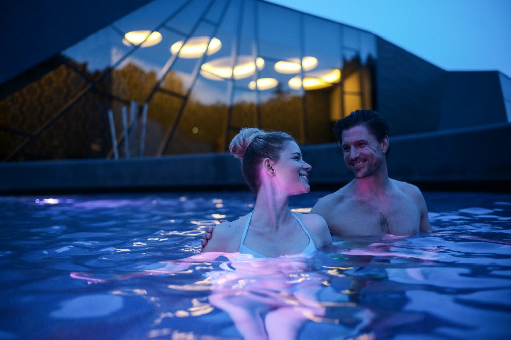 A romantic couple bathing in an outdoor pool at Wellness Orhidelia thermal spa at night